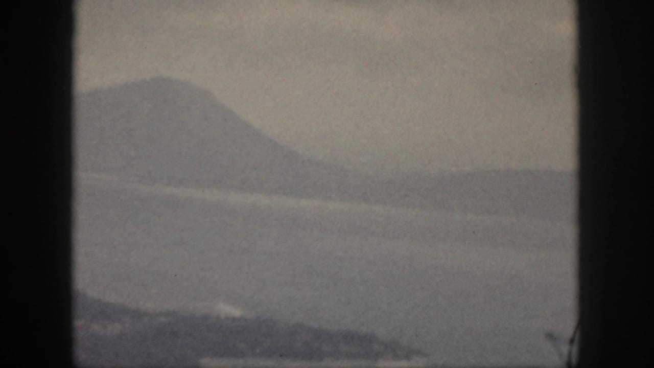 1959 Oahu 8mm frame showing misty water and distant green mountain ridges through a dark window-like border.