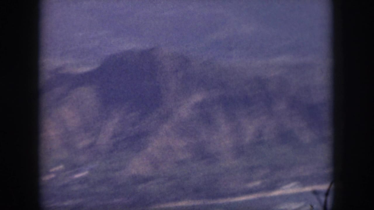 Soft 8mm Oahu frame with blue-toned mountain slopes, shoreline traces, and a dark vertical border in the foreground.