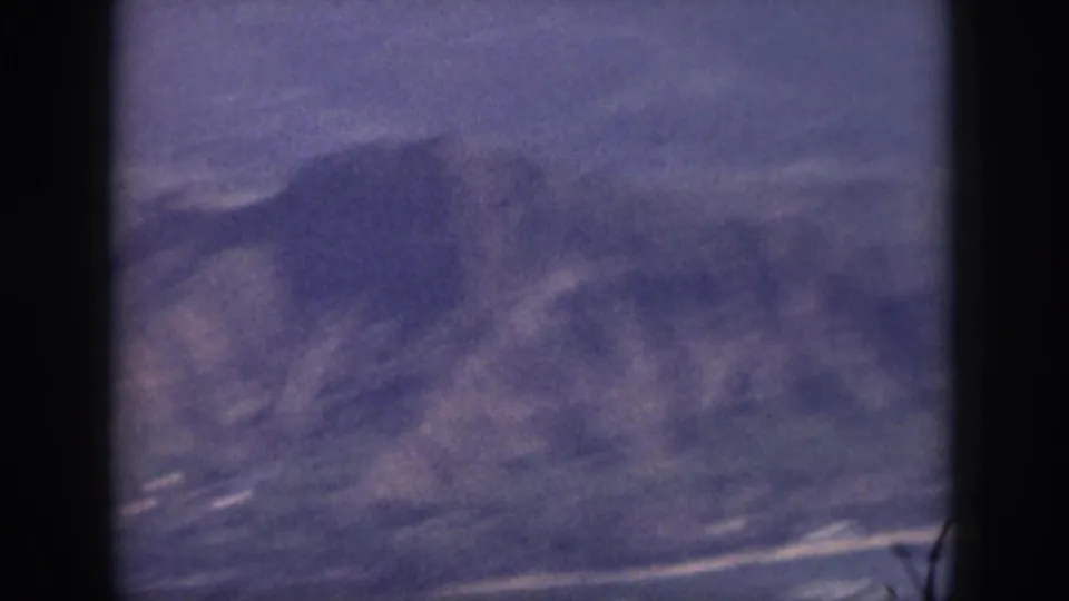 Soft 8mm Oahu frame with blue-toned mountain slopes, shoreline traces, and a dark vertical border in the foreground.