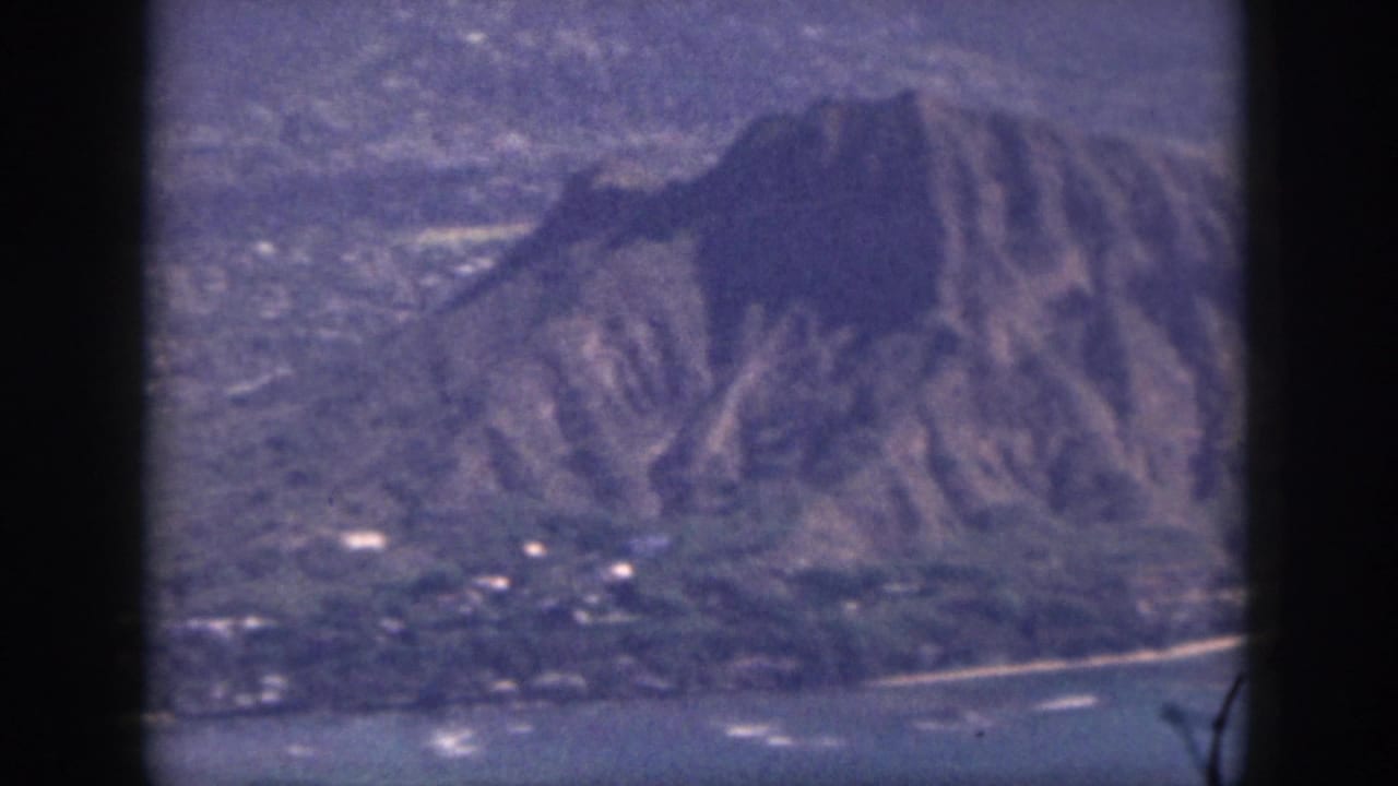 1959 Oahu frame showing a rugged volcanic peak above shoreline, coastal water, and dark window-like borders.