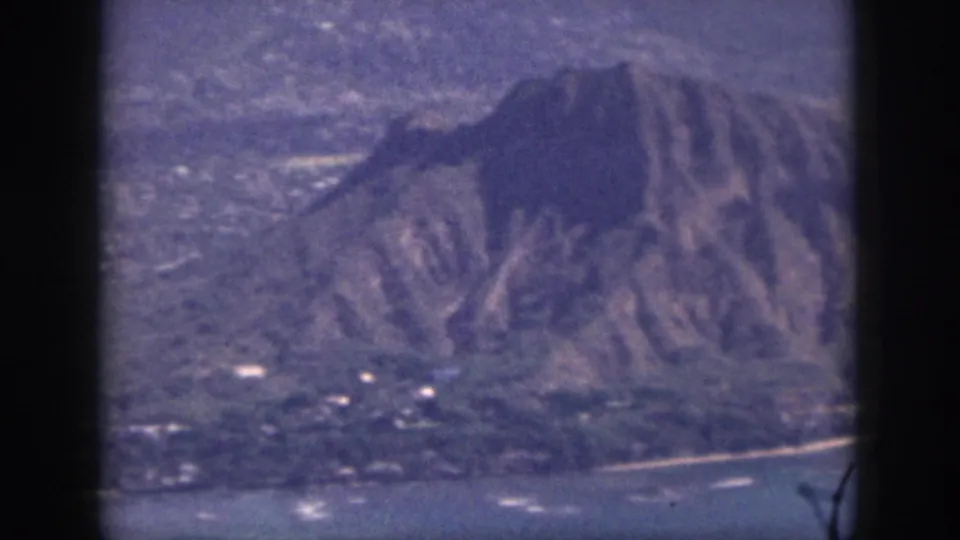 1959 Oahu frame showing a rugged volcanic peak above shoreline, coastal water, and dark window-like borders.