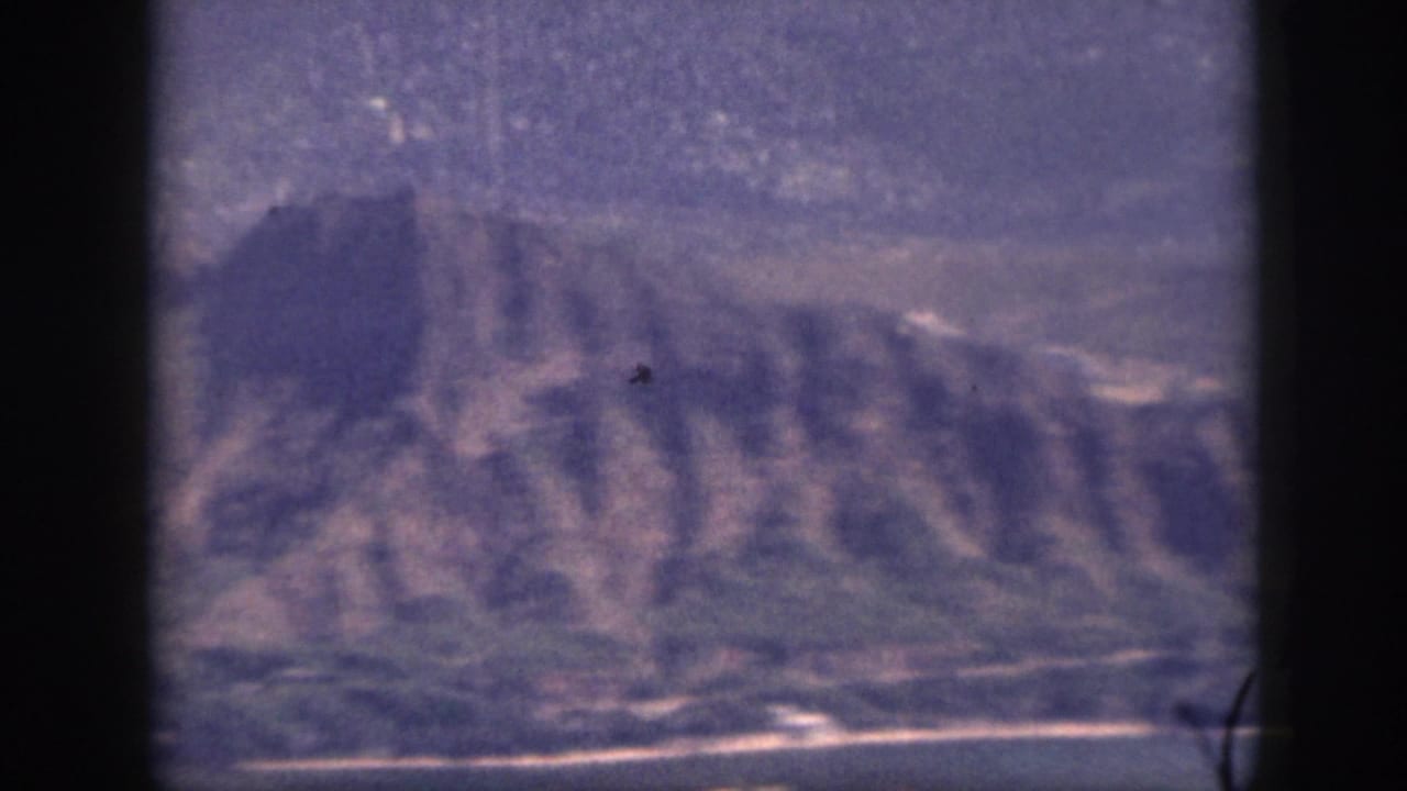1959 Oahu 8mm frame showing a rugged ridge descending toward a pale beach and waterline.
