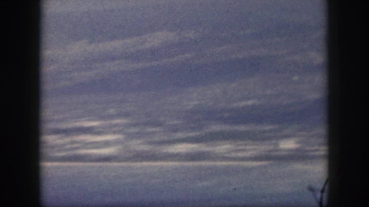 Blue ocean and distant mountain slopes viewed through dark vertical framing.