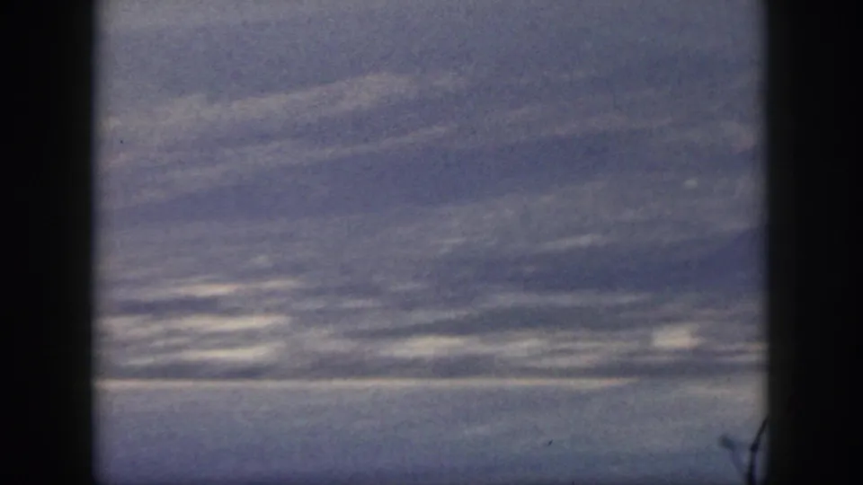 1959 Oahu footage frame with ocean water, distant mountain ridges, and soft atmospheric haze behind dark vertical frame bars.