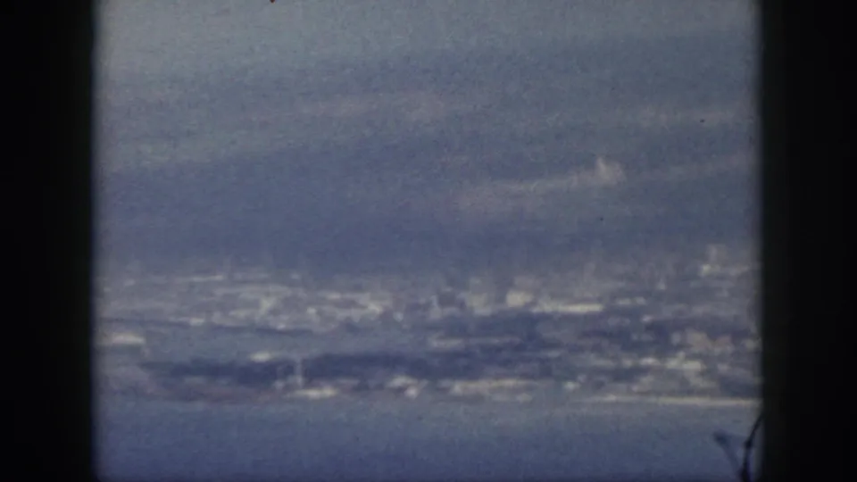 1959 Oahu frame with a distant coastal city, ocean water, and atmospheric haze seen through dark 8mm framing.