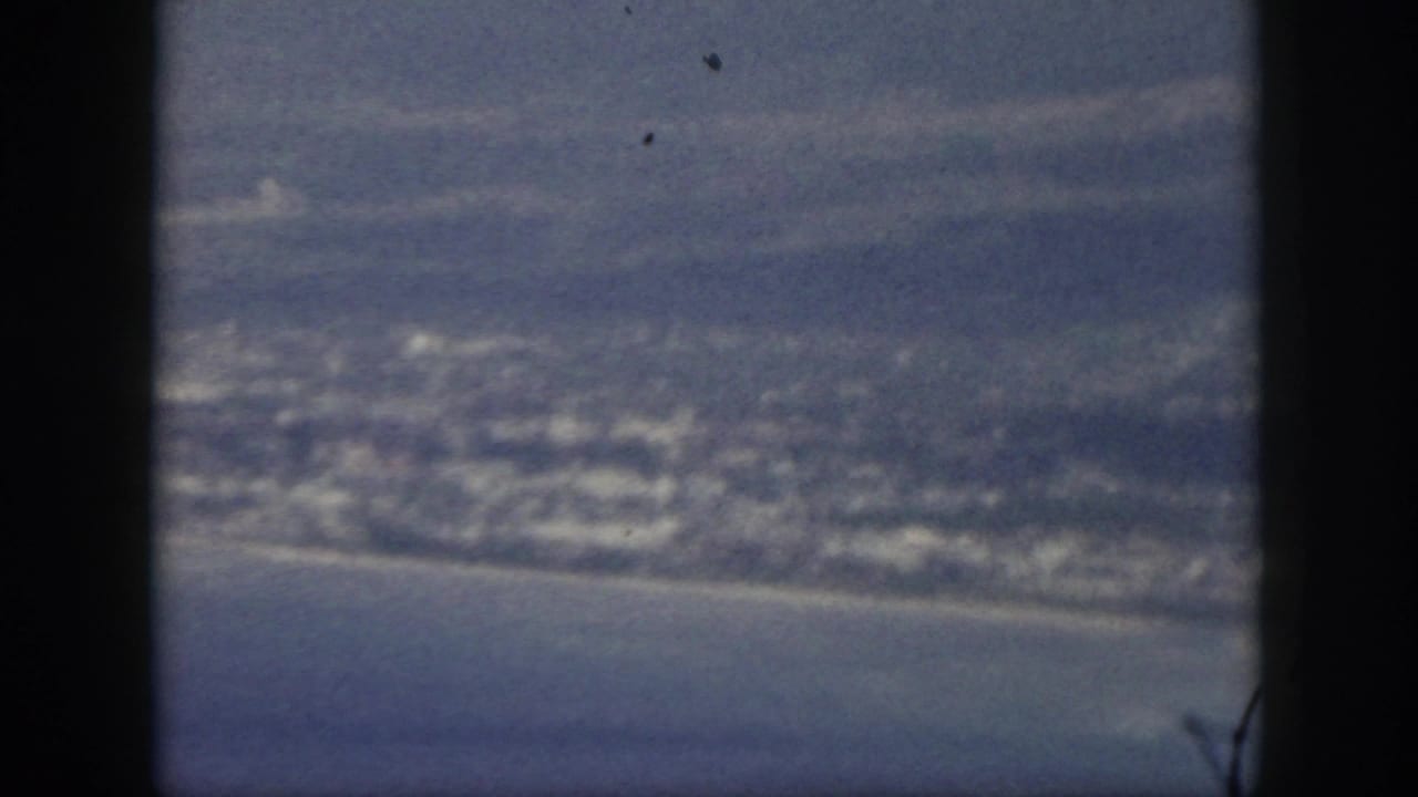 1959 Oahu aerial frame with a coastal town, curved shoreline, ocean, and aircraft window edge.