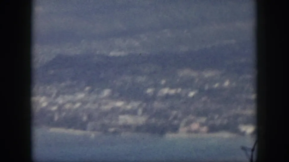 1959 Oahu coastal settlement and shoreline seen from above, with mountains in haze and a dark vertical band crossing the frame.