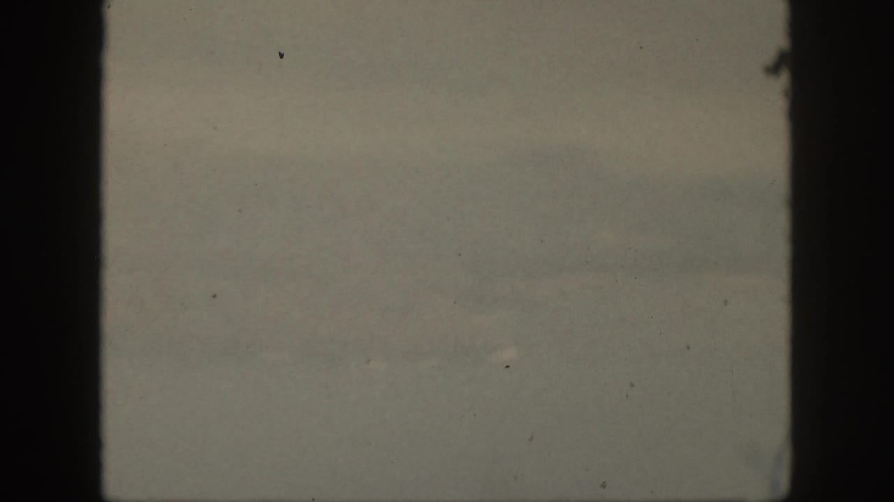 Faint ocean horizon and muted sky within a dark film border.