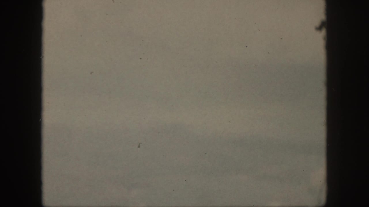 Soft, faded Oahu home-movie frame with pale ocean, haze, and the visible dark 8mm film gate.