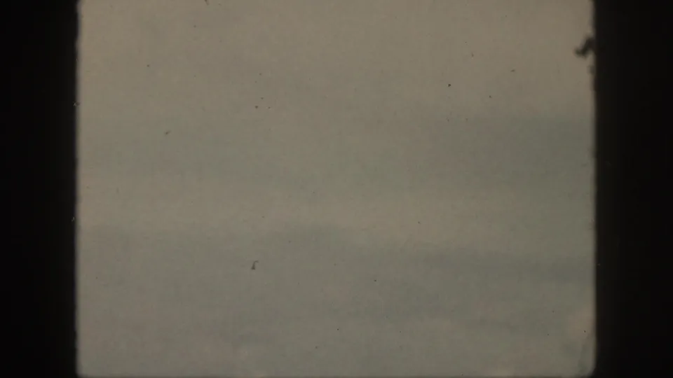 Soft, faded Oahu home-movie frame with pale ocean, haze, and the visible dark 8mm film gate.