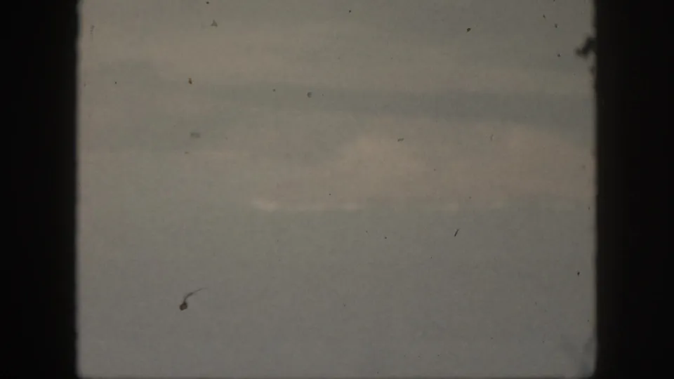 1959 Oahu 8mm frame showing a dim, overcast sky with soft cloud bands, black gate edges, visible dust, and muted color.