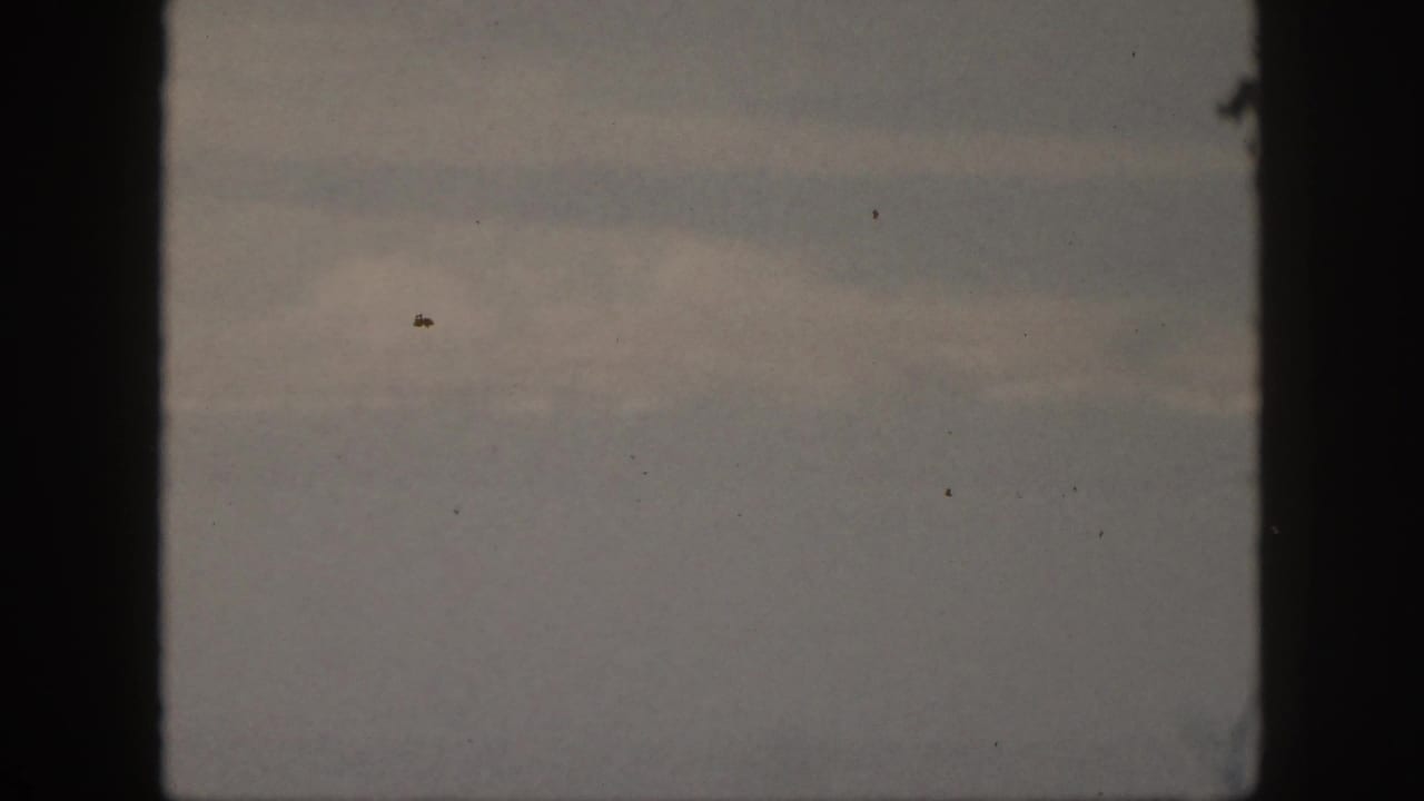 Dark overcast sky with pale cloud bands, film grain, dust, and black side borders.