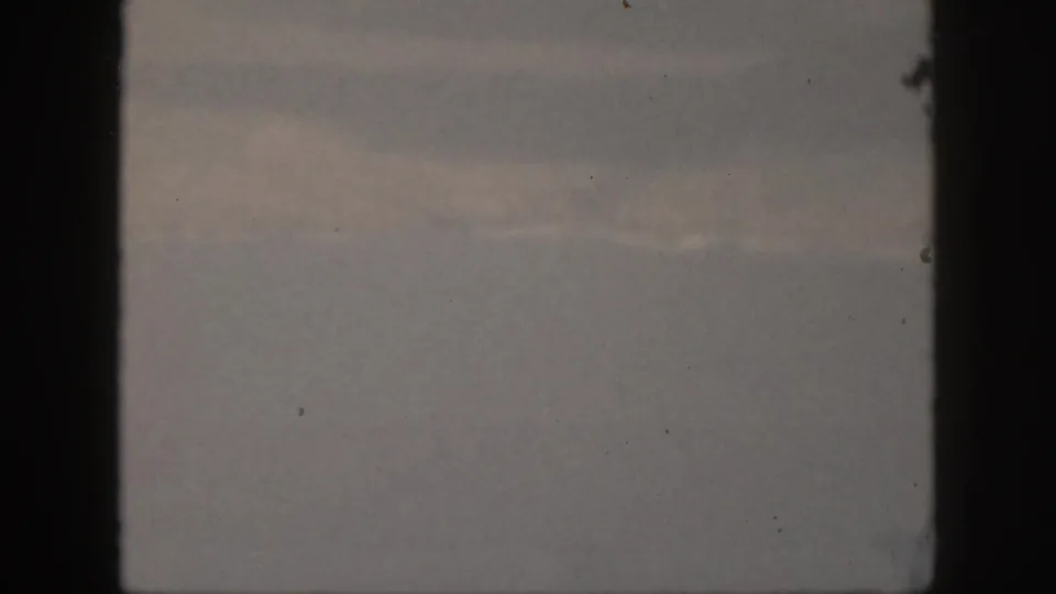 1959 Oahu 8mm still showing blue-gray cloud cover, subdued light patches, black frame edges, grain, and small dust marks.