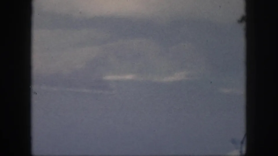 1959 Oahu 8mm frame showing layered dark clouds with small bright breaks, blue-gray tones, dust specks, and heavy black gate borders.
