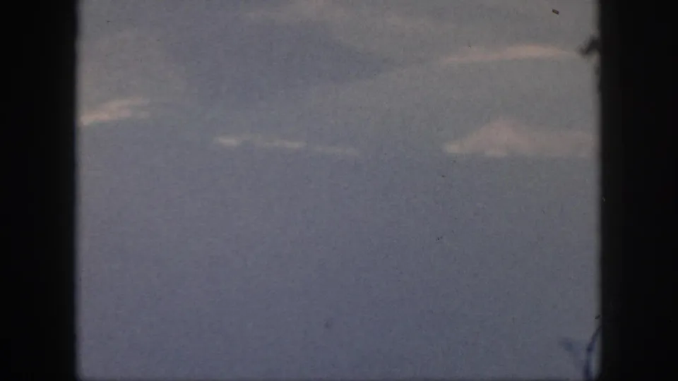 1959 Oahu travel footage frame showing a muted ocean-and-sky view through dark aircraft window framing.