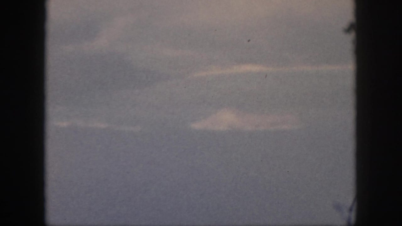 1959 Oahu home-movie frame with wispy clouds and blue-gray sea or sky seen from an airplane window.