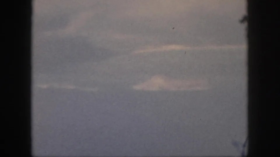 1959 Oahu home-movie frame with wispy clouds and blue-gray sea or sky seen from an airplane window.