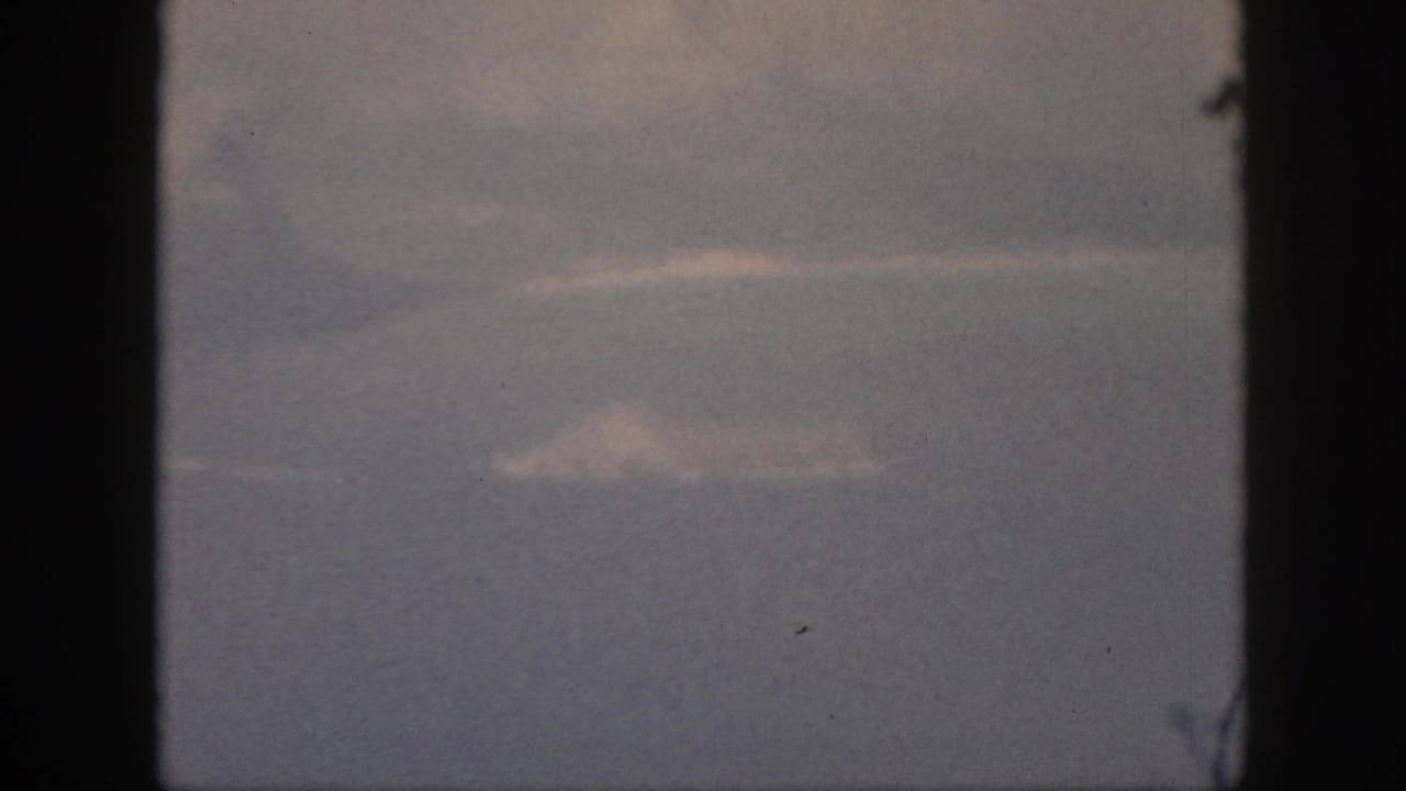 1959 Oahu frame from inside an aircraft, showing pale cloud forms over a blue-gray sea or sky through the window.