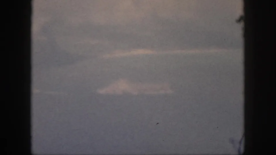 1959 Oahu frame from inside an aircraft, showing pale cloud forms over a blue-gray sea or sky through the window.
