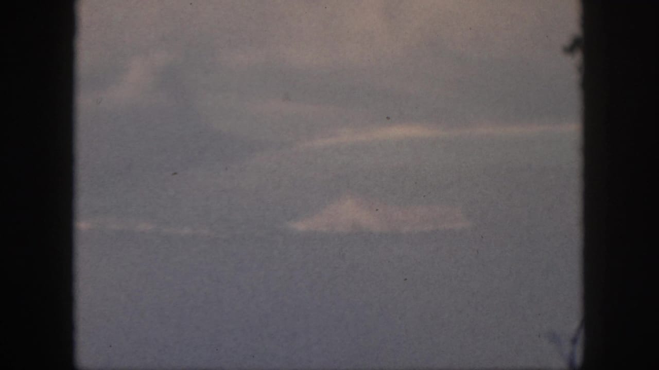 1959 8mm home-movie view from an airplane window, showing muted haze and low clouds with no visible ground landmark.