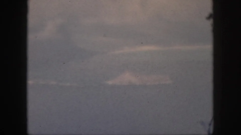 1959 8mm home-movie view from an airplane window, showing muted haze and low clouds with no visible ground landmark.