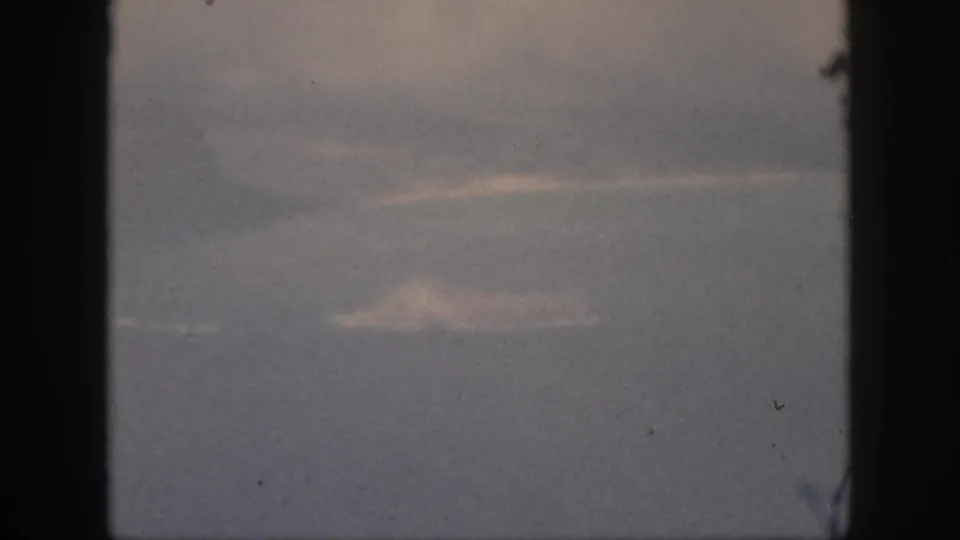 Aircraft-window view from 1959 Hawaii travel footage, with pale cloud shapes and a dark window edge dominating the frame.