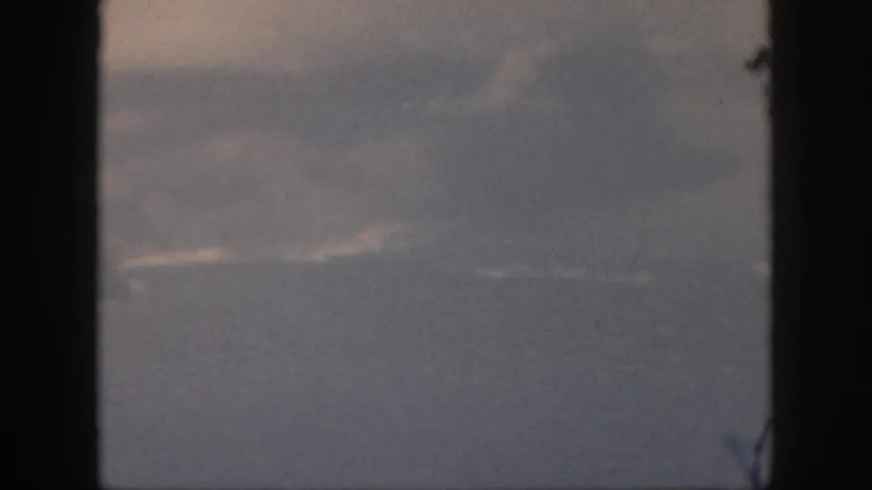 8mm airplane passenger view with blue-gray haze, faint cloud bands, and heavy dark window framing.