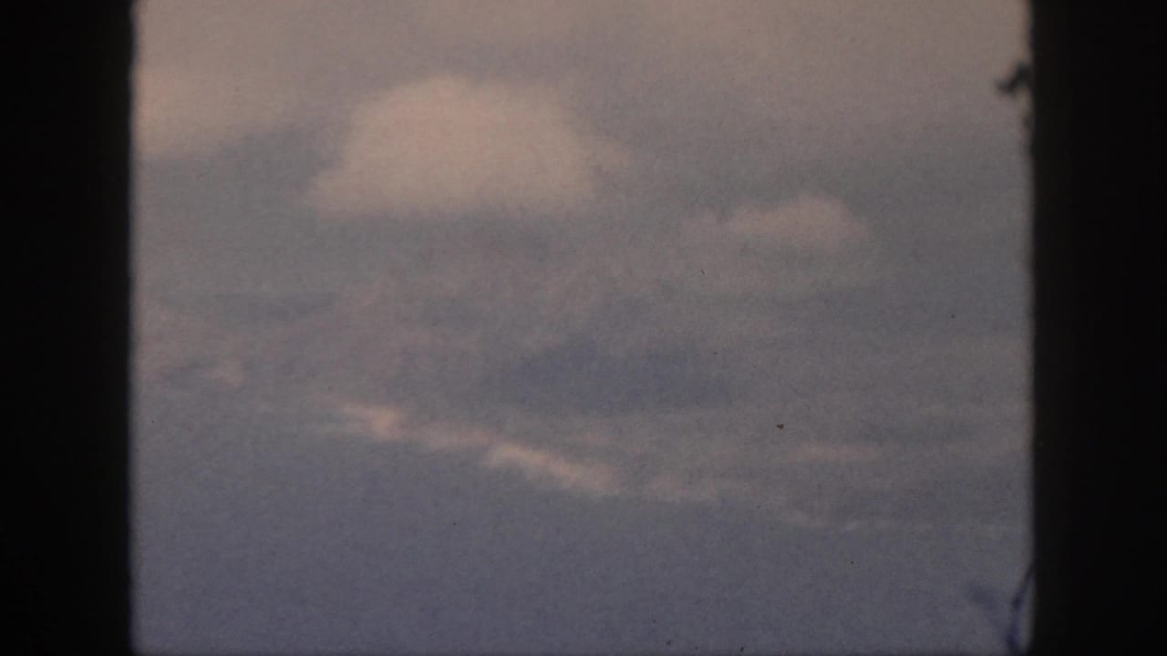 Late-1950s 8mm travel footage shows a pale cloud mass and layered haze through the aircraft window.