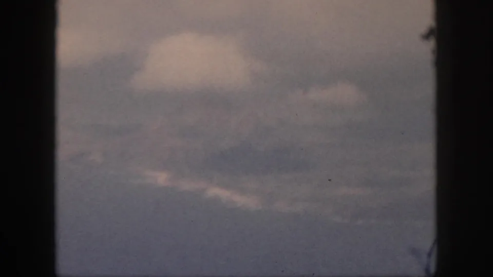 Late-1950s 8mm travel footage shows a pale cloud mass and layered haze through the aircraft window.