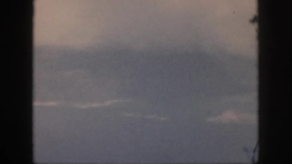 A faded 8mm frame from Oahu shows a hazy aerial view through window bars, with faint cloud bands and indistinct terrain or water.