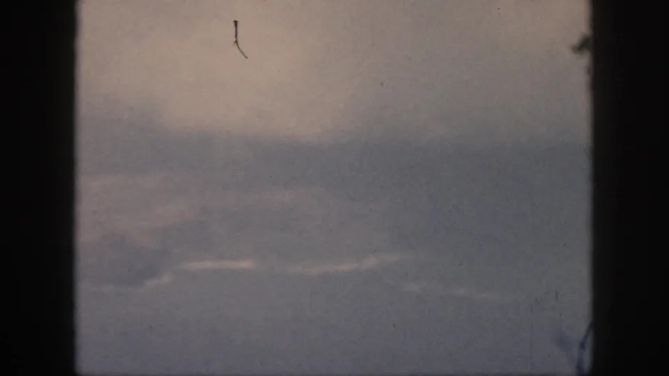 The final 1959 Oahu frame holds on a hazy aerial scene through a dark aircraft window, with pale cloud streaks and visible 8mm dust.
