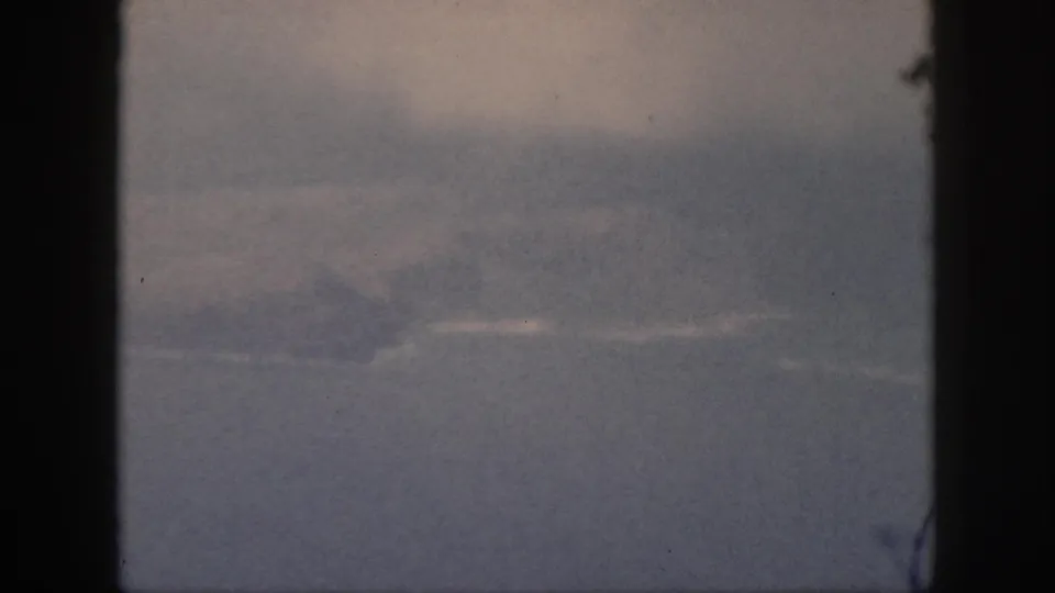 1959 Oahu home-movie frame showing a hazy ocean horizon and faint landform through dark vertical window edges.