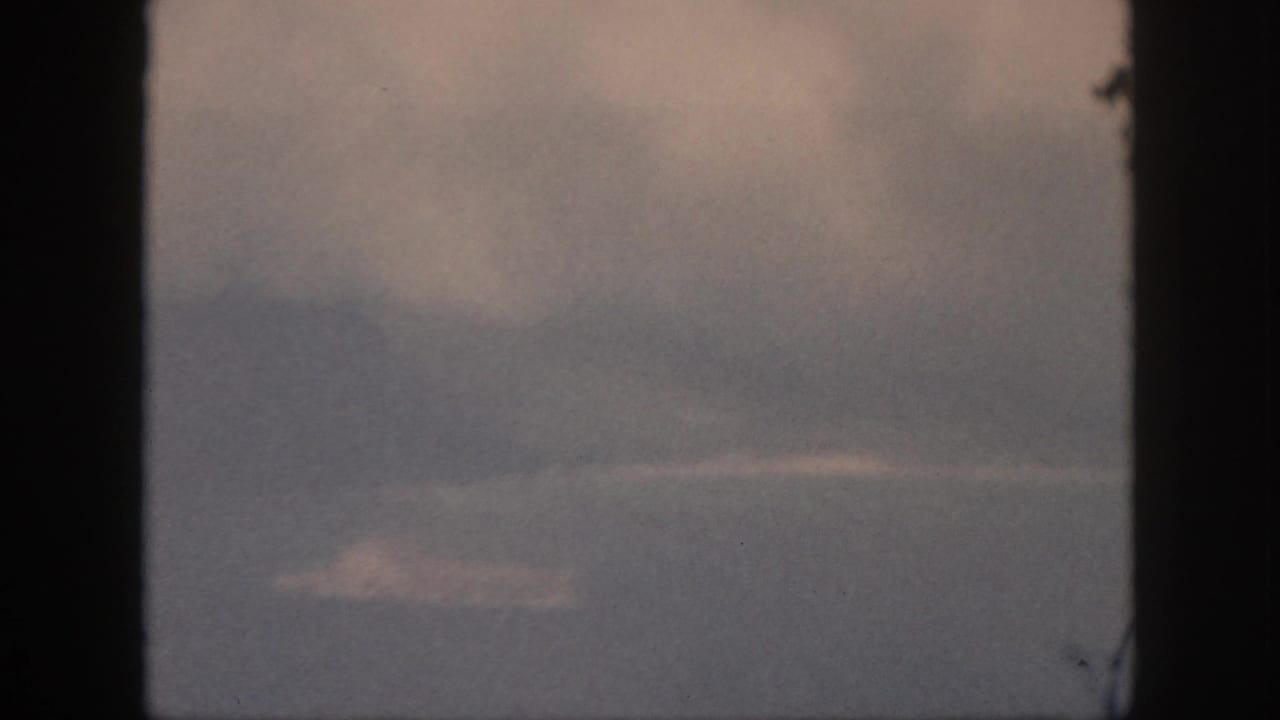 1959 Oahu home-movie frame with cloudy sky, faint land, and dark window edges enclosing the ocean horizon.