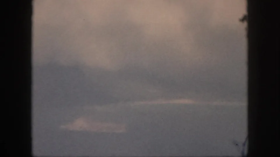 1959 Oahu home-movie frame with cloudy sky, faint land, and dark window edges enclosing the ocean horizon.