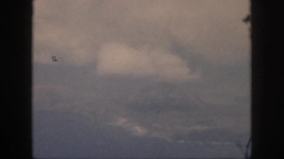 1959 Oahu 8mm aerial view with pale clouds and a muted sky framed by dark vertical film borders.