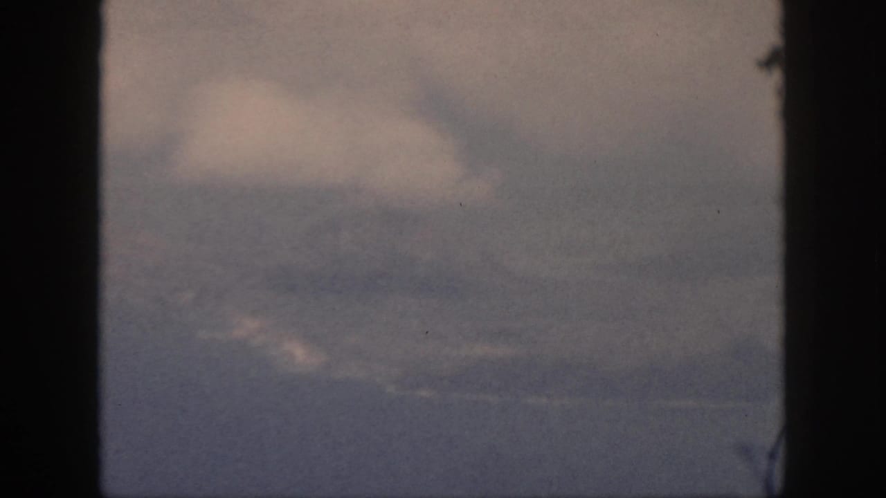 1959 Oahu 8mm frame showing a low haze line, layered cloud, and possible distant water or coast beneath the sky.