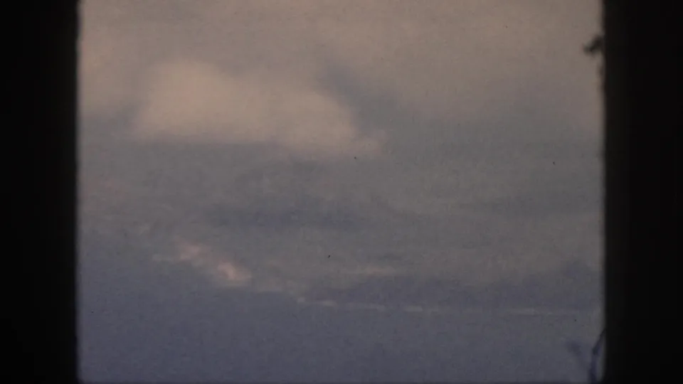 1959 Oahu 8mm frame showing a low haze line, layered cloud, and possible distant water or coast beneath the sky.