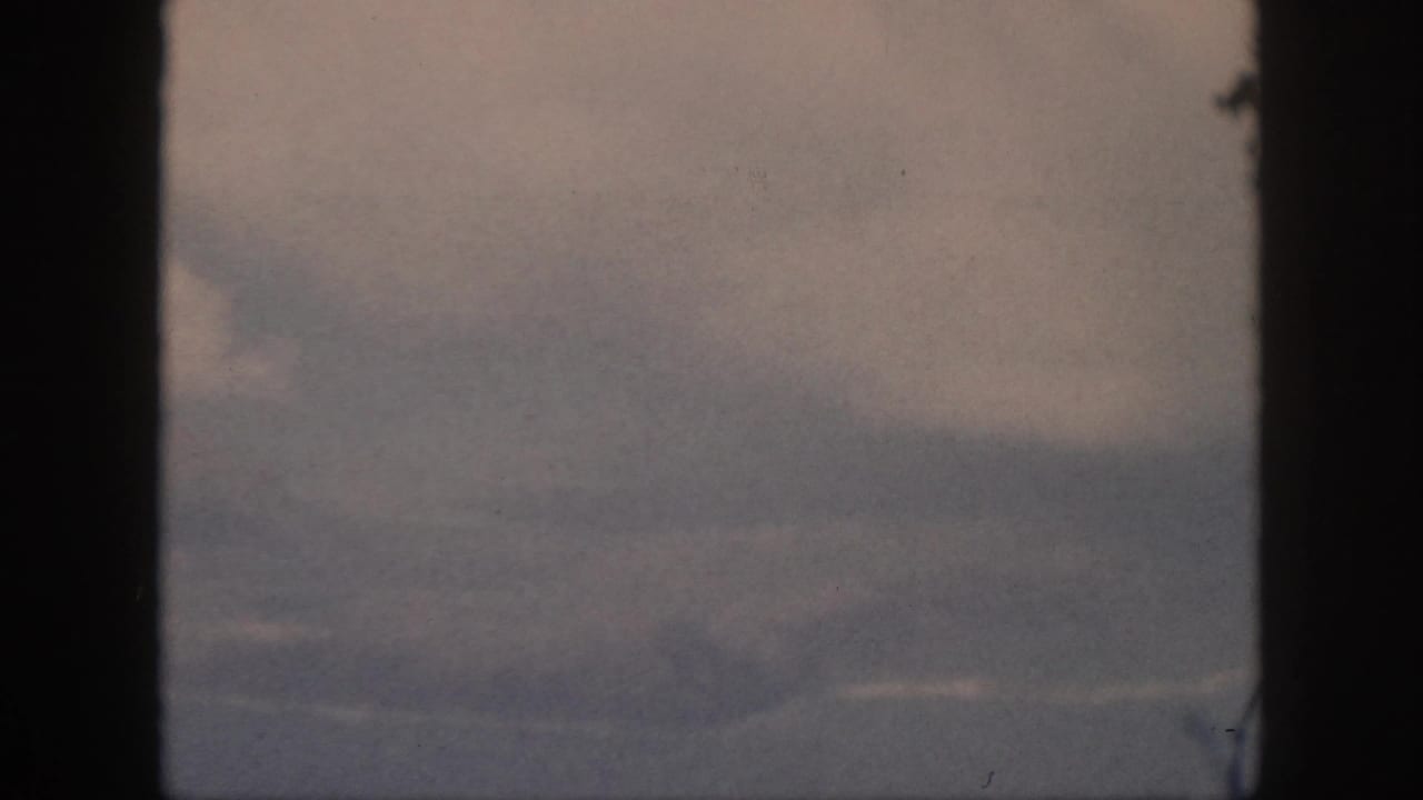 1959 Oahu 8mm aerial frame with a large pale cloud, hazy sky, and indistinct coastline or water at the lower edge.