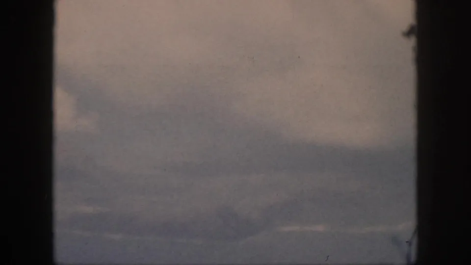 1959 Oahu 8mm aerial frame with a large pale cloud, hazy sky, and indistinct coastline or water at the lower edge.