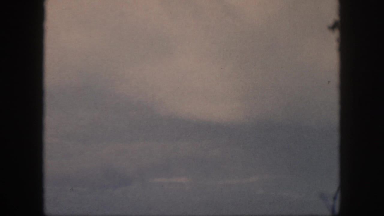 1959 Oahu travel footage showing muted cloud layers viewed through a dark airplane window frame.