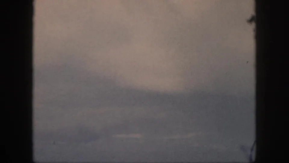 1959 Oahu travel footage showing muted cloud layers viewed through a dark airplane window frame.