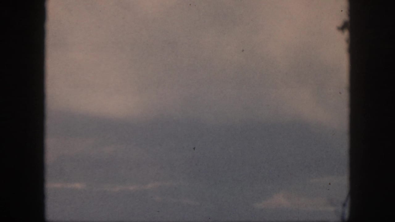 Muted 1959 in-flight view near Oahu, with cloud bands divided by the dark airplane window structure.