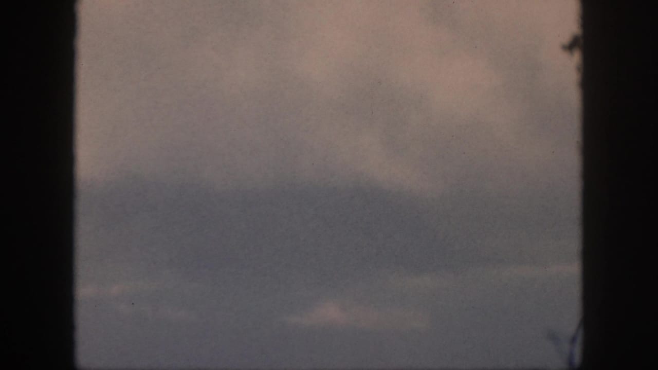 Home-movie airplane-window view from 1959 Oahu footage, showing soft overcast cloud layers and faded color.