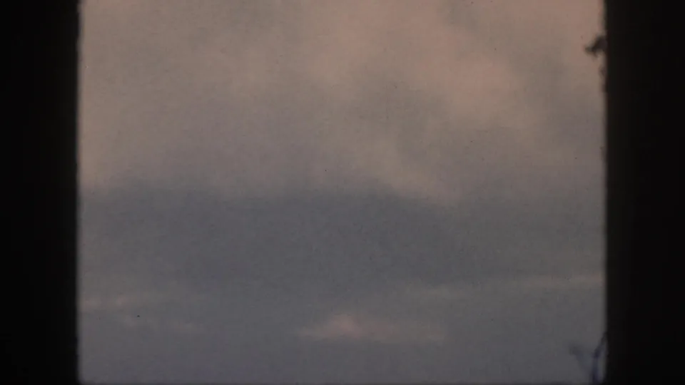 Home-movie airplane-window view from 1959 Oahu footage, showing soft overcast cloud layers and faded color.