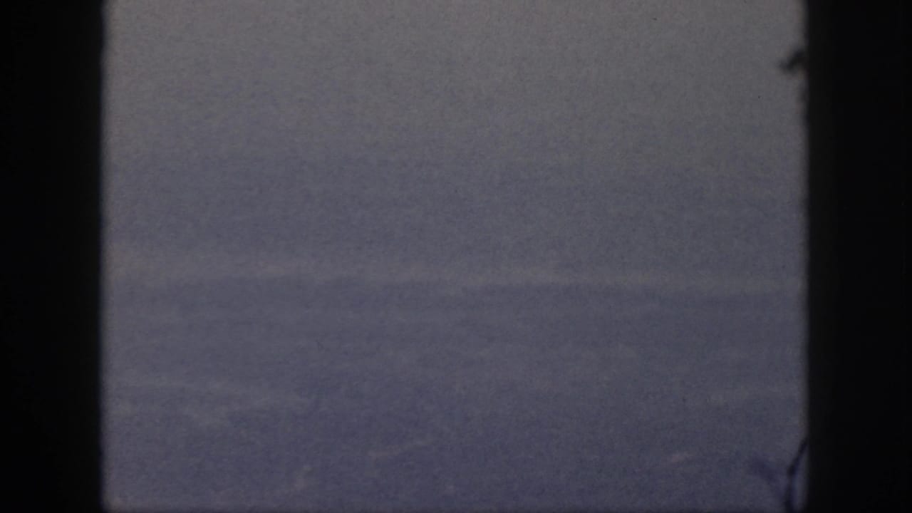 Blue-gray cloud layers in 1959 Oahu travel footage, framed by dark aircraft-window edges and visible film grain.