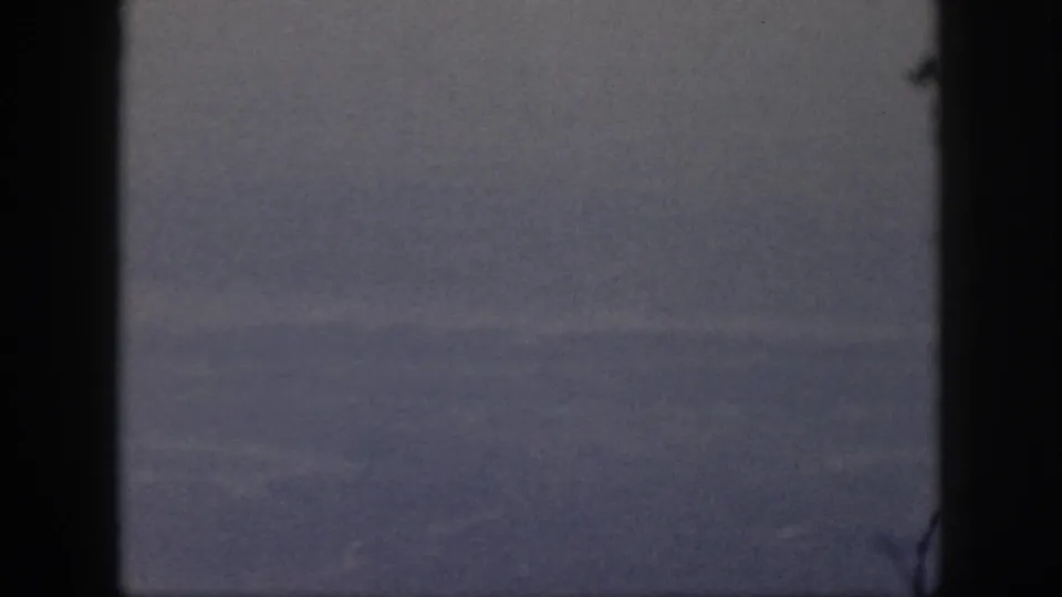 Blue-gray cloud layers in 1959 Oahu travel footage, framed by dark aircraft-window edges and visible film grain.