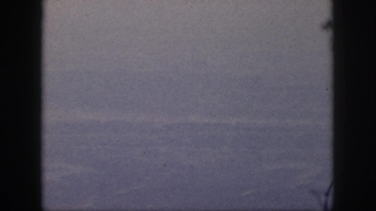 Soft aerial landscape seen between dark vertical window edges.