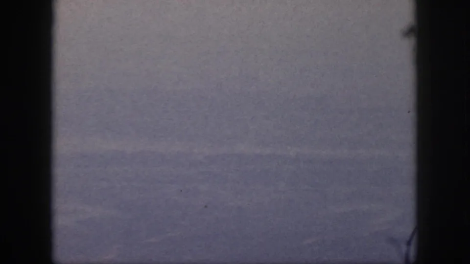 A muted 1959 Oahu aerial view appears between dark airplane-window edges, with soft focus and visible film grain.