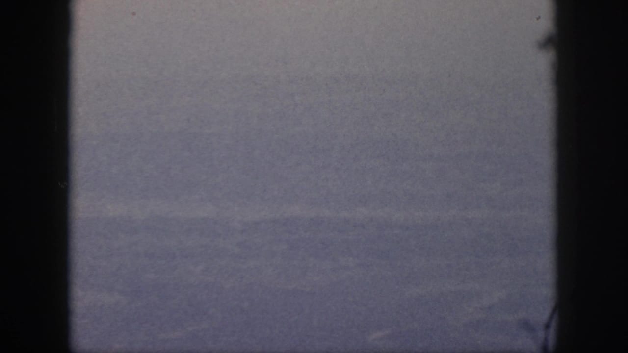 The 8mm frame shows blurred ground far below, bordered by the dark airplane window during the 1959 Oahu flight.