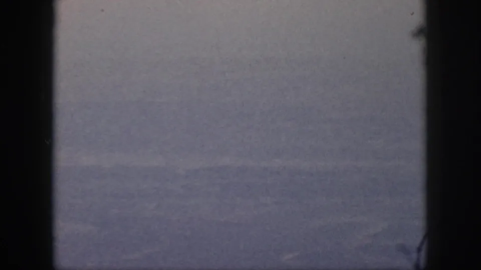 The 8mm frame shows blurred ground far below, bordered by the dark airplane window during the 1959 Oahu flight.